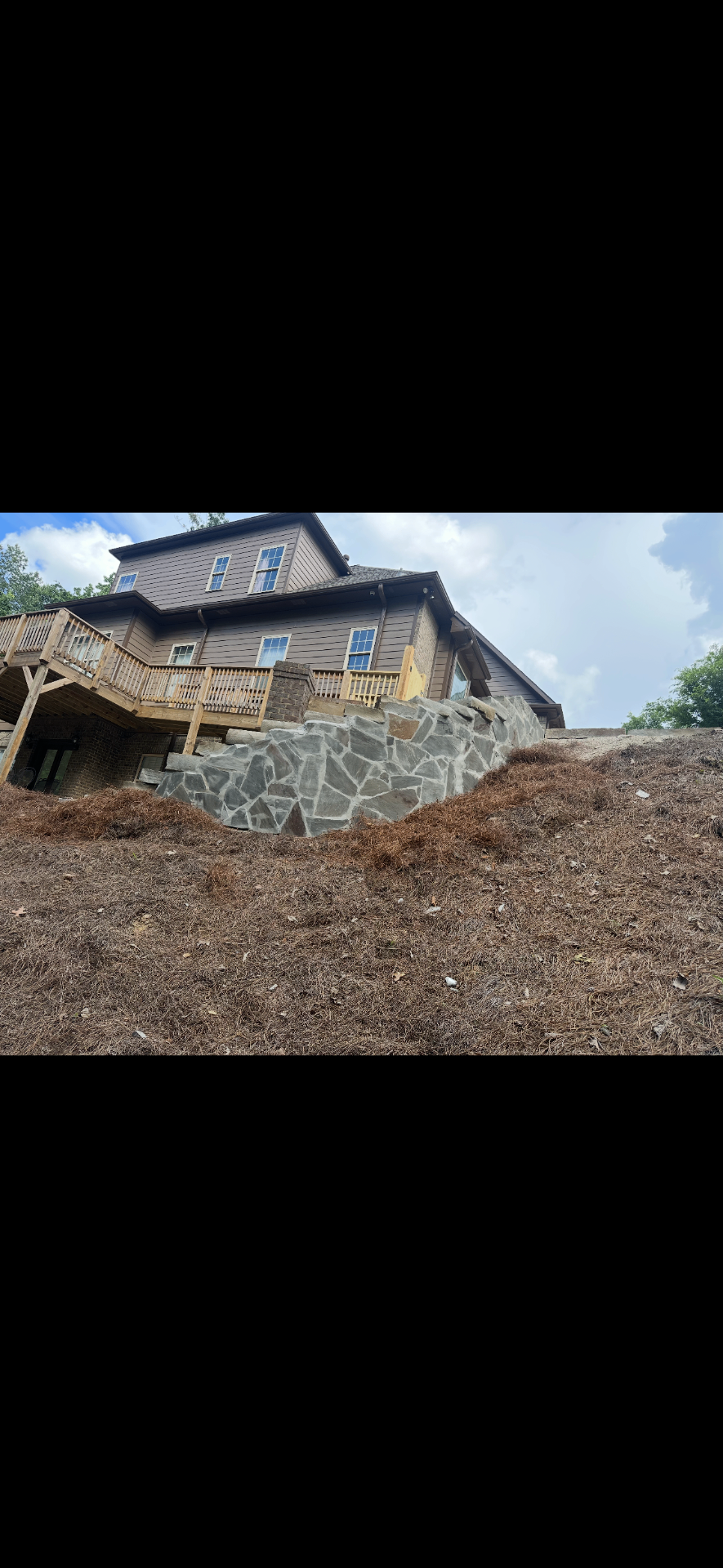 Tall custom stone retaining wall supporting a hillside below a home